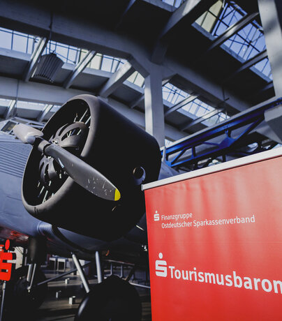Rotes Roll-up des Sparkassen-Tourismusbarometers vor einem historischen Junckers-Flugzeug in Dessau